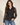 A woman modeling a black leopard-print button-up blouse with sheer long sleeves, paired with blue jeans, against a plain beige studio background.
