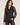 A woman modeling a black leopard-print button-up shirt with sheer long sleeves, paired with black jeans, against a plain light beige studio background.