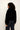 A model shown from the back wearing a black cropped faux fur jacket with a high collar and dark blue jeans, set against a plain off-white background.