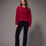 a woman wearing a brushed v-neck red sweater and black jeans on a grey studio background.