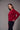 a woman wearing a brushed v-neck red sweater and black jeans on a grey studio background.