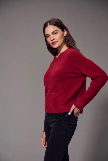a woman wearing a brushed v-neck red sweater and black jeans on a grey studio background.