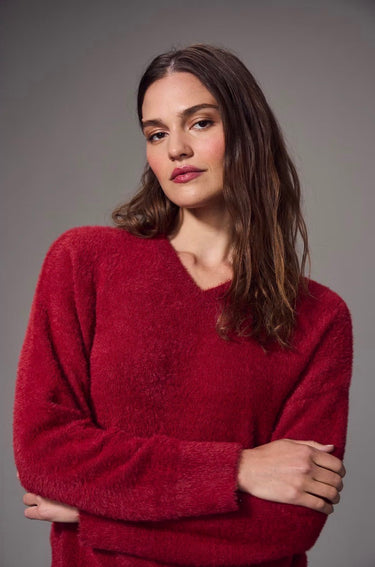 a woman wearing a brushed v-neck red sweater and black jeans on a grey studio background.