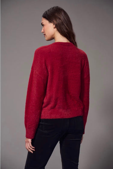 a woman wearing a brushed v-neck red sweater and black jeans on a grey studio background.