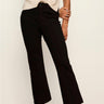 A model wearing black cropped flare pants, paired with a cream short-sleeve top and black pointed-toe heels, standing against a plain off-white wall.