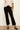A model wearing black cropped flare pants, paired with a cream short-sleeve top and black pointed-toe heels, standing against a plain off-white wall.