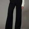 A woman wearing a black ponte pants and a white sweater on a studio background