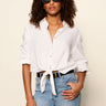 Woman wearing a white button-up shirt and blue jeans with sunglasses on a beige background