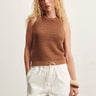 Woman wearing a brown sleeveless knitted top and white pants against a light background