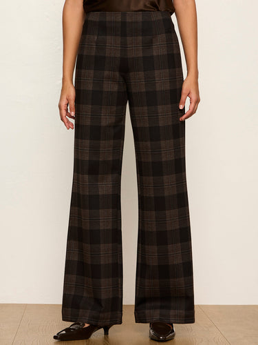 A model is shown from the waist down wearing high-waisted, wide-leg plaid trousers in a dark brown and black pattern, paired with black pointed-toe heels against a neutral cream background.
