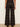 A person shown from the back wearing dark brown and black plaid wide-leg trousers, standing against a plain off-white wall on a light wood floor.