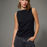 A woman wearing a black boatneck rhinestone tank and black jeans on a grey studio background.