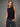 A woman wearing a black boatneck rhinestone tank and black jeans on a grey studio background.