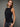 A woman wearing a black boatneck rhinestone tank and black jeans on a grey studio background.