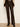 A person wearing dark brown faux-leather flare pants with a ribbed knit sweater and black boots, standing against a plain off-white wall.