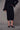 a woman wearing a black sweater with feather cuffs, a mesh midi skirt with a velvet floral pattern and black heels on a grey studio background