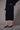 a woman wearing a black sweater with feather cuffs, a mesh midi skirt with a velvet floral pattern and black heels on a grey studio background