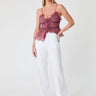 Woman wearing a pink ruffled top and white pants on a white background