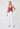 Woman wearing a pink ruffled top and white pants on a white background