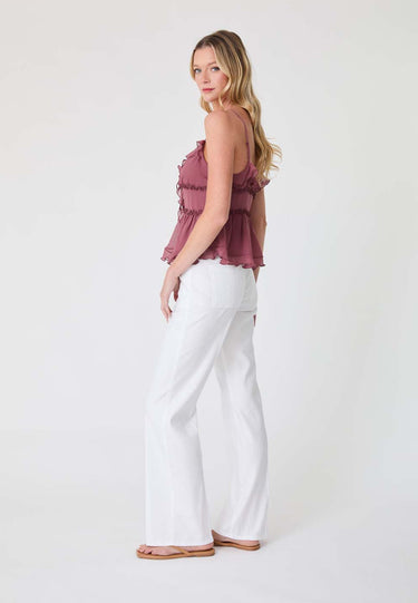 Woman wearing a mauve top and white pants on a white background