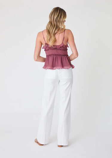 Woman wearing a pink ruffled top and white pants on a white background