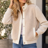A woman wearing a multi textured jacket with fuzzy and ribbed textures outside.