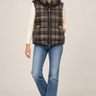 a woman wearing jeans, a white long sleeve top and a plaid vest on a white background.