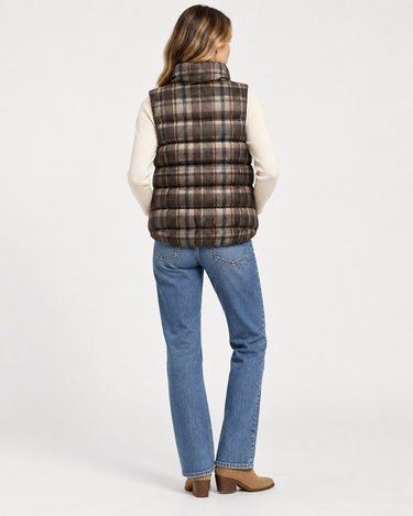 a woman wearing jeans, a white long sleeve top and a plaid vest on a white background.