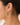A close-up of a model's ear wearing a delicate silver hoop earring adorned with small pale green and yellow beads and white pearl-like accents.
