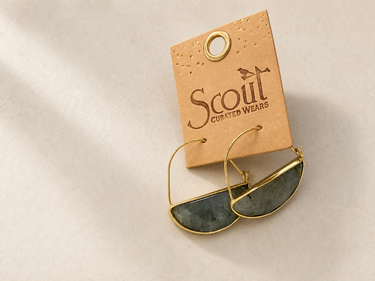 Gold hoop earrings with dark gray stone inlays, attached to a tan paper display card printed with the Scout Curated Wears logo, on a neutral beige background.