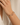A close-up of a person's wrist wearing three delicate beaded bracelets, including a gold chain and strands of small multicolored beads, against a soft cream-colored background.