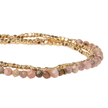 A close-up of a multi-strand beaded bracelet featuring gold-toned metallic beads and faceted light pink gemstone beads, set against a plain white background.