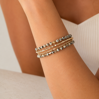A close-up of a person's wrist wearing three stacked beaded bracelets, including gold-tone and gray-blue marbled bead strands.