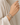 A close-up of a person's wrist wearing three beaded stretch bracelets in neutral tones of beige, gray, and white, styled with a cream-colored top.