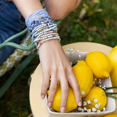 Hand with beaded bracelets on a bowl of lemons outdoors