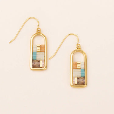 Gold-framed earrings with multicolored stones on a beige background