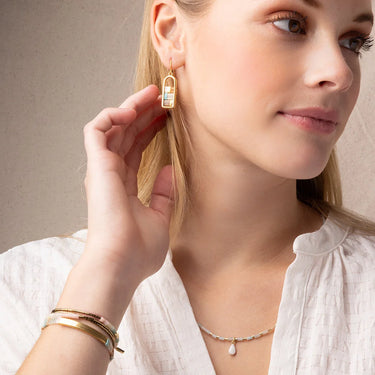 Woman wearing gold earrings and bracelets with a neutral background