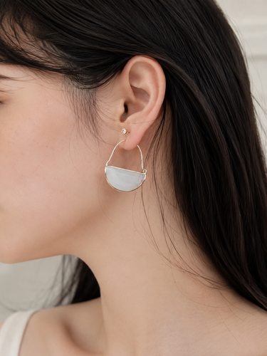 A close-up side profile of a woman wearing a delicate silver hoop earring with a large, semi-circular white stone drop pendant.