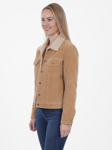 A woman wearing a tan suede jacket with a cream sherpa collar and dark blue jeans, shown from the waist up against a plain white studio background.