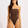 Woman wearing a brown swimsuit with white trim on a light pink background