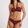 A front view of a wrap halter burgundy swim top on a model on a white background