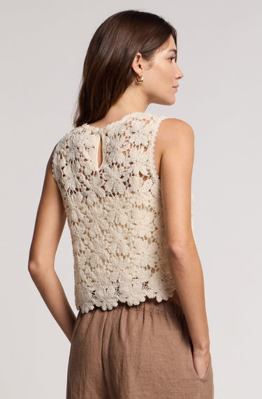 A woman wearing an oat colored crochet floral top and beige pants