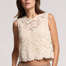 A woman wearing an oat colored crochet floral top and beige pants