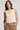 A woman wearing an oat colored crochet floral top and beige pants