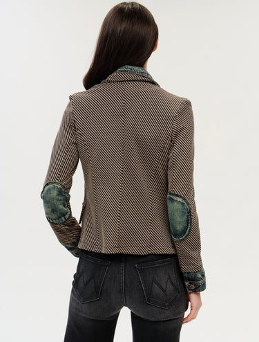 A woman facing backwards wearing a checkered blazer with denim elbow patches on a white background.