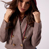 A woman wearing a cropped houndstooth blazer in brown and beige with gold buttons, a burgundy hood, and blue jeans, posing against a light gray studio background.