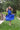 Woman in a blue dress standing on grass with trees in the background