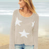 Woman wearing a light brown sweater with white star patterns on a beach.