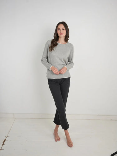 a woman wearing a light grey charcoal sweater with black jeans on a white background