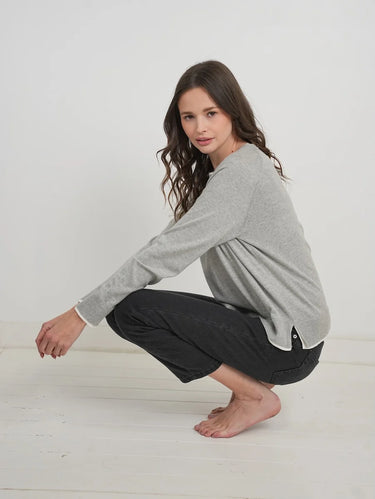 a woman wearing a light grey charcoal sweater with black jeans on a white background